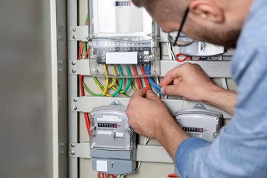 Photo of Man checking connecting cables on electricity meter indoors, closeup view