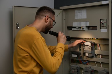 Man with flashlight checking electricity meter indoors