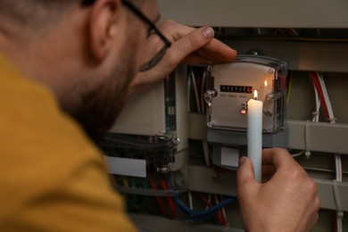 Photo of Man with candle checking electricity meter indoors, closeup