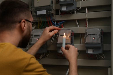 Photo of Man with candle checking electricity meter indoors