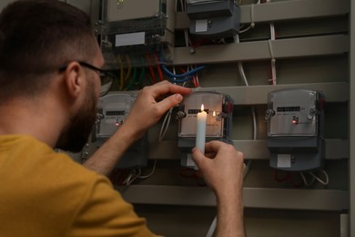 Man with candle checking electricity meter indoors