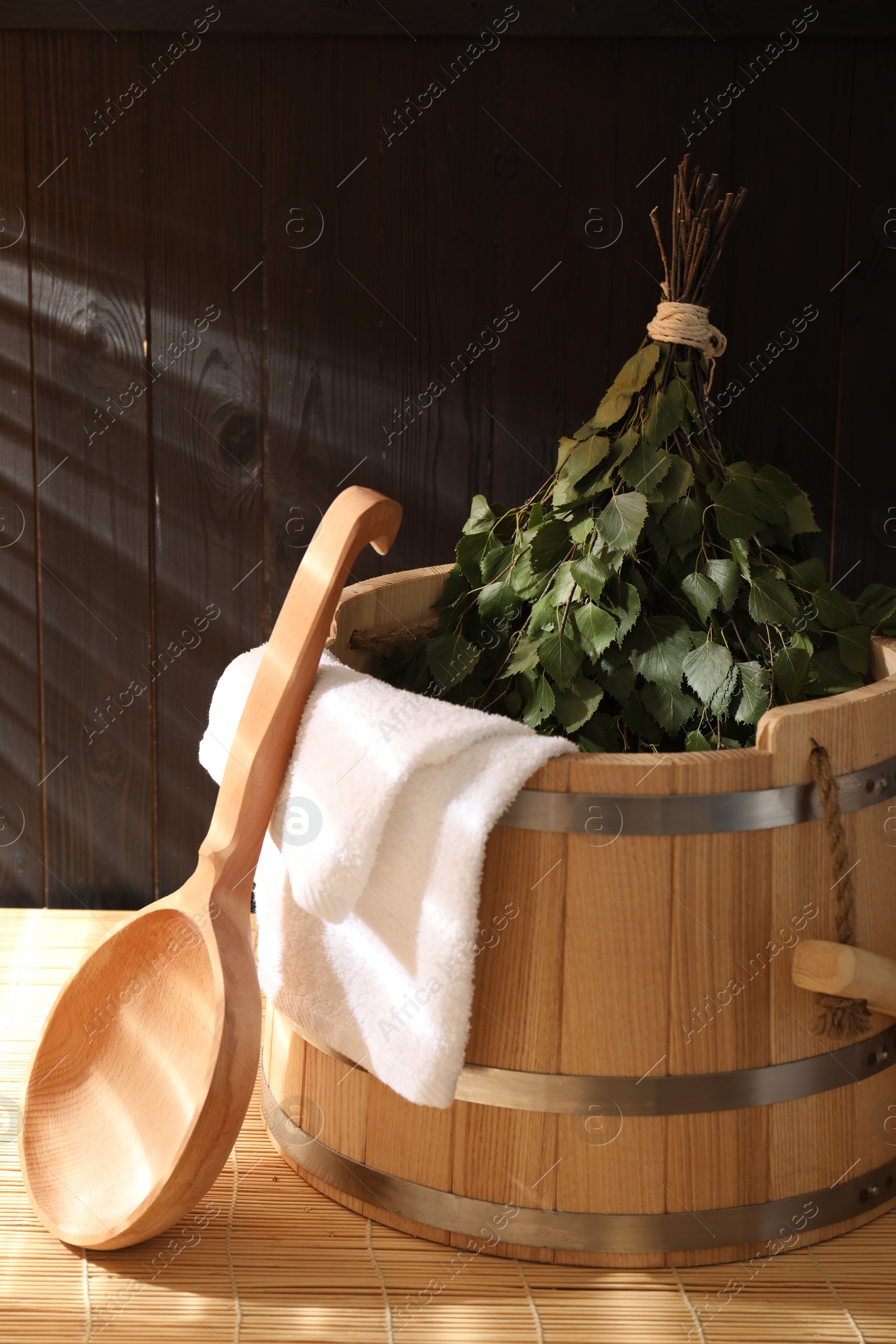 Photo of Sauna equipment. Bucket, ladle, birch whisk and towel on bamboo bench indoors