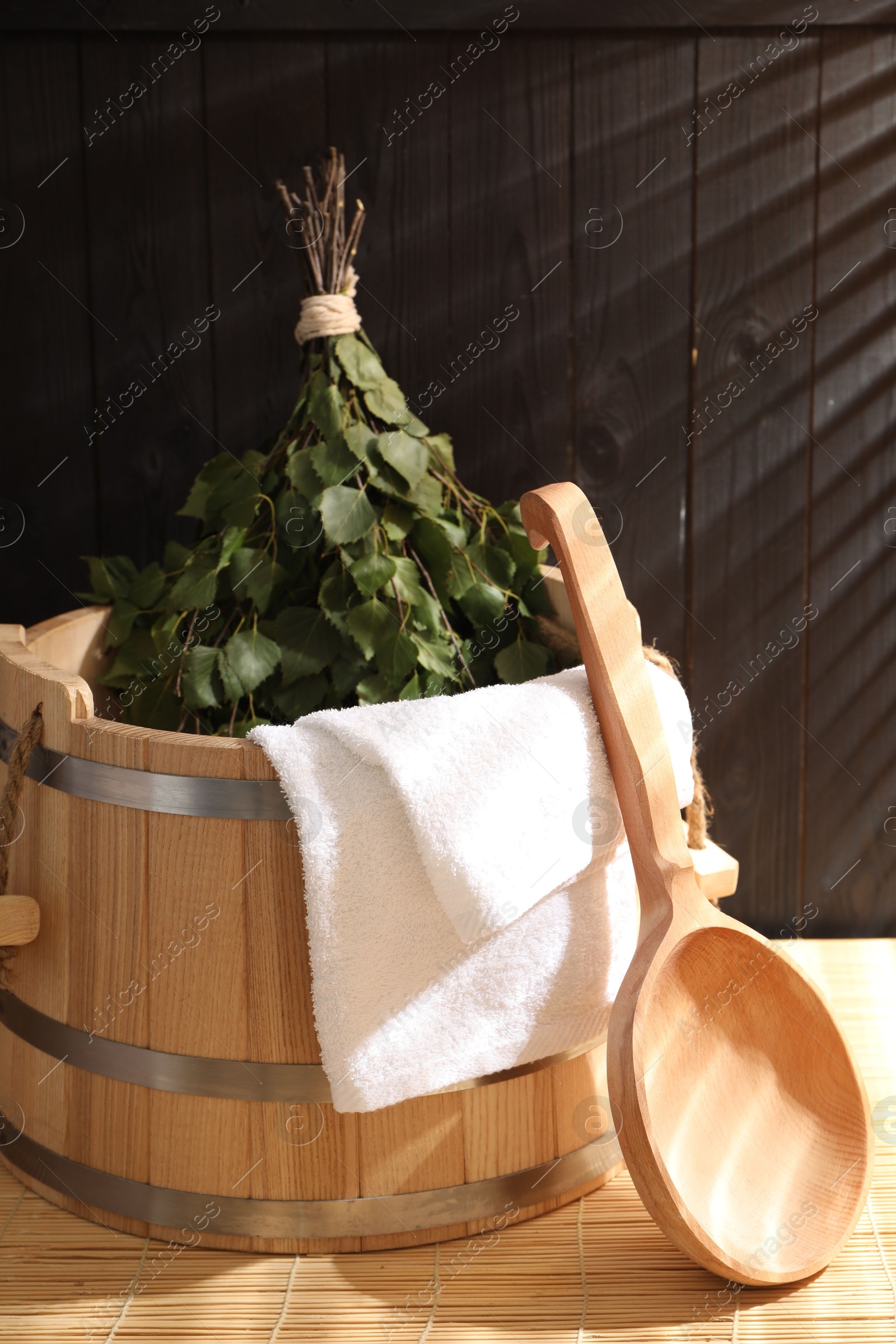 Photo of Sauna equipment. Bucket, ladle, birch whisk and towel on bamboo bench indoors