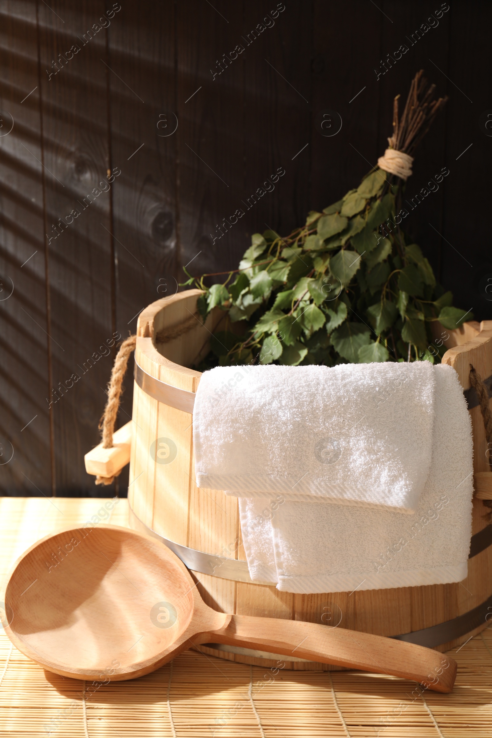 Photo of Sauna equipment. Bucket, ladle, birch whisk and towel on bamboo bench indoors