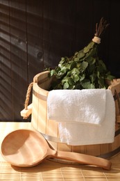 Photo of Sauna equipment. Bucket, ladle, birch whisk and towel on bamboo bench indoors