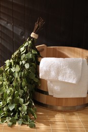 Photo of Sauna equipment. Bucket, birch whisk and towel on bamboo bench indoors