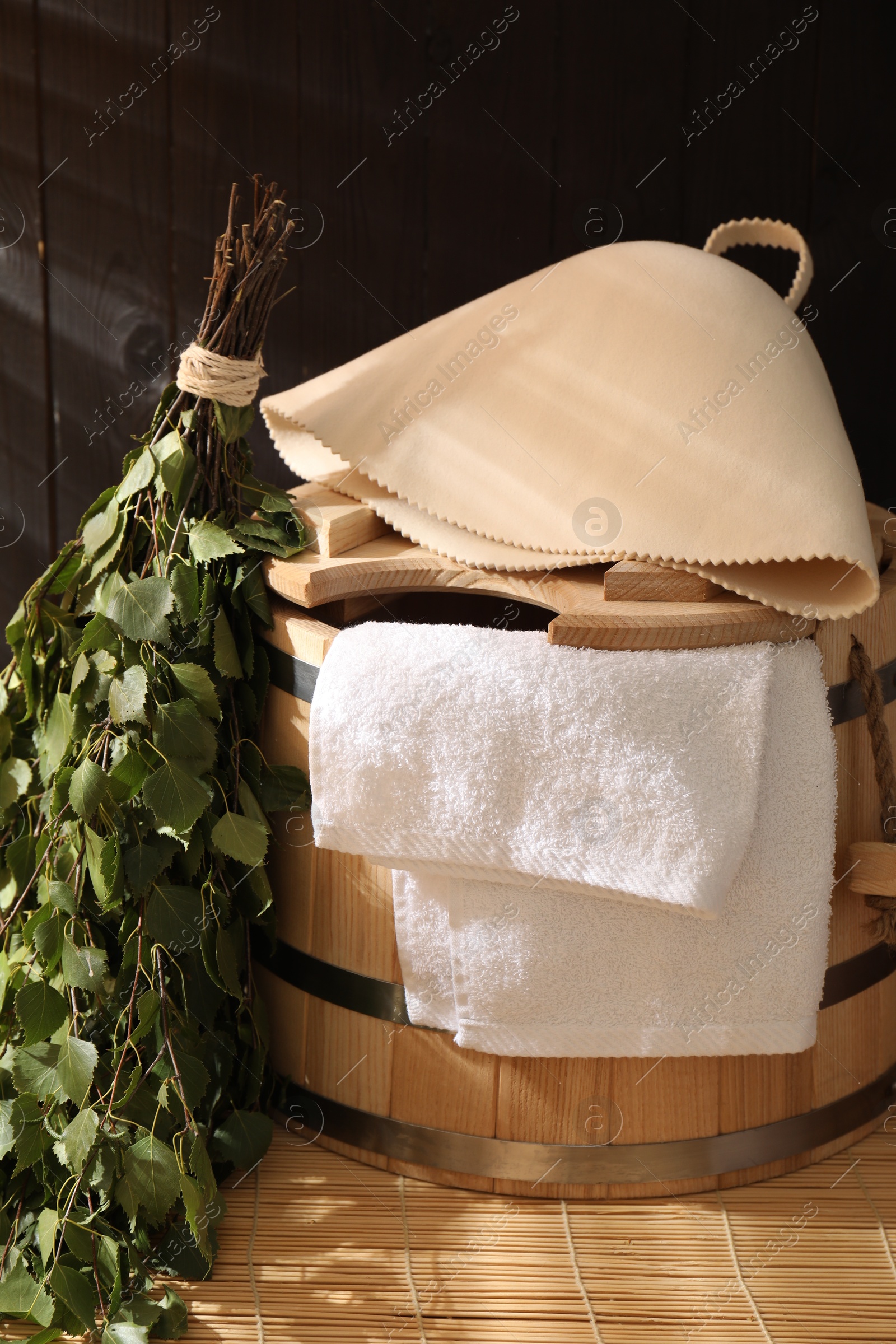 Photo of Sauna equipment. Bucket, felt wool hat, birch whisk and towel on bamboo bench indoors