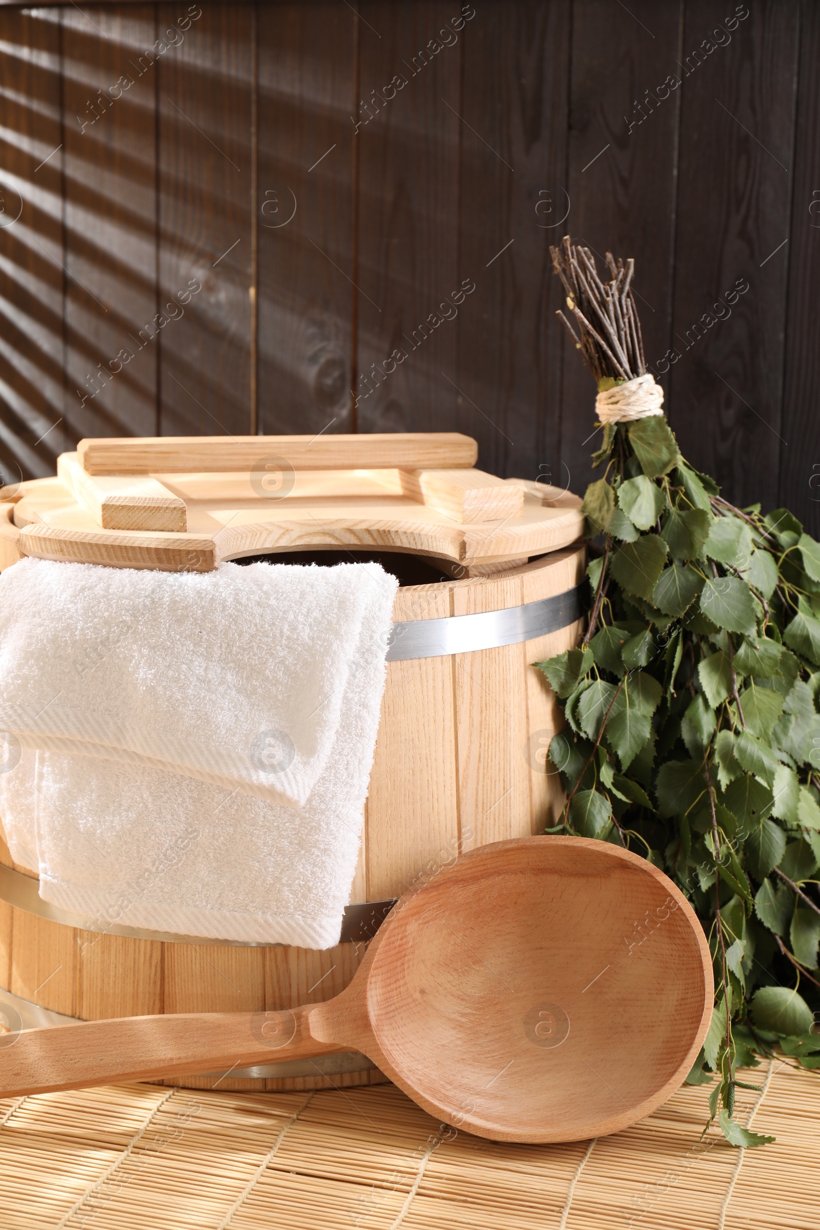 Photo of Sauna equipment. Bucket, ladle, birch whisk and towel on bamboo bench indoors