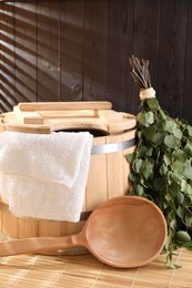 Photo of Sauna equipment. Bucket, ladle, birch whisk and towel on bamboo bench indoors