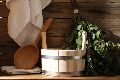 Sauna equipment. Bucket, ladle, birch whisk and towels on wooden table indoors