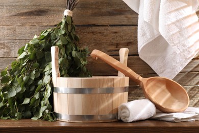 Photo of Sauna equipment. Bucket, ladle, birch whisk and towels on wooden table indoors