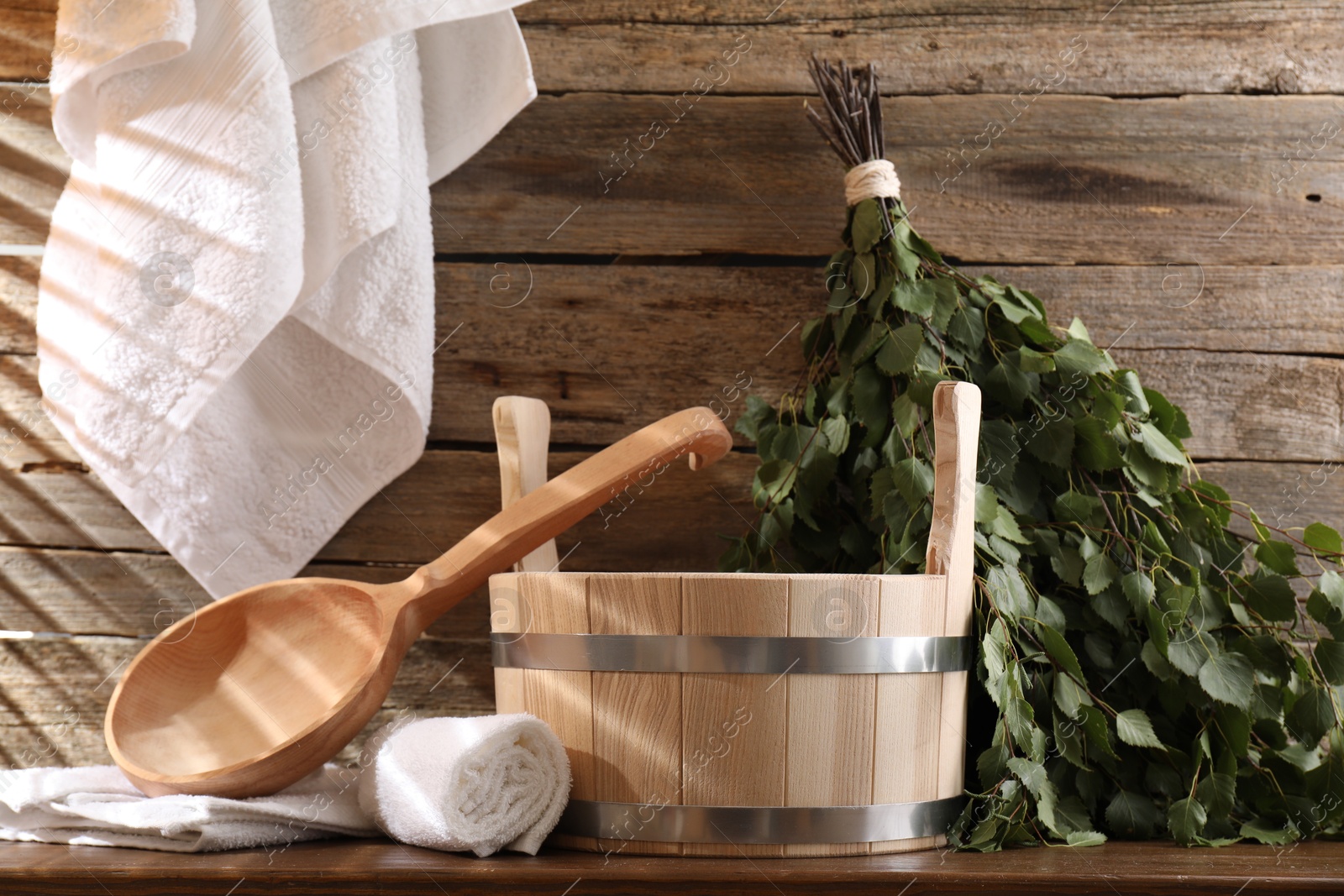 Photo of Sauna equipment. Bucket, ladle, birch whisk and towels on wooden table indoors