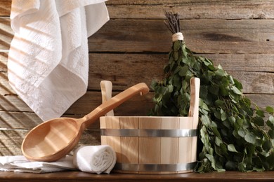 Photo of Sauna equipment. Bucket, ladle, birch whisk and towels on wooden table indoors