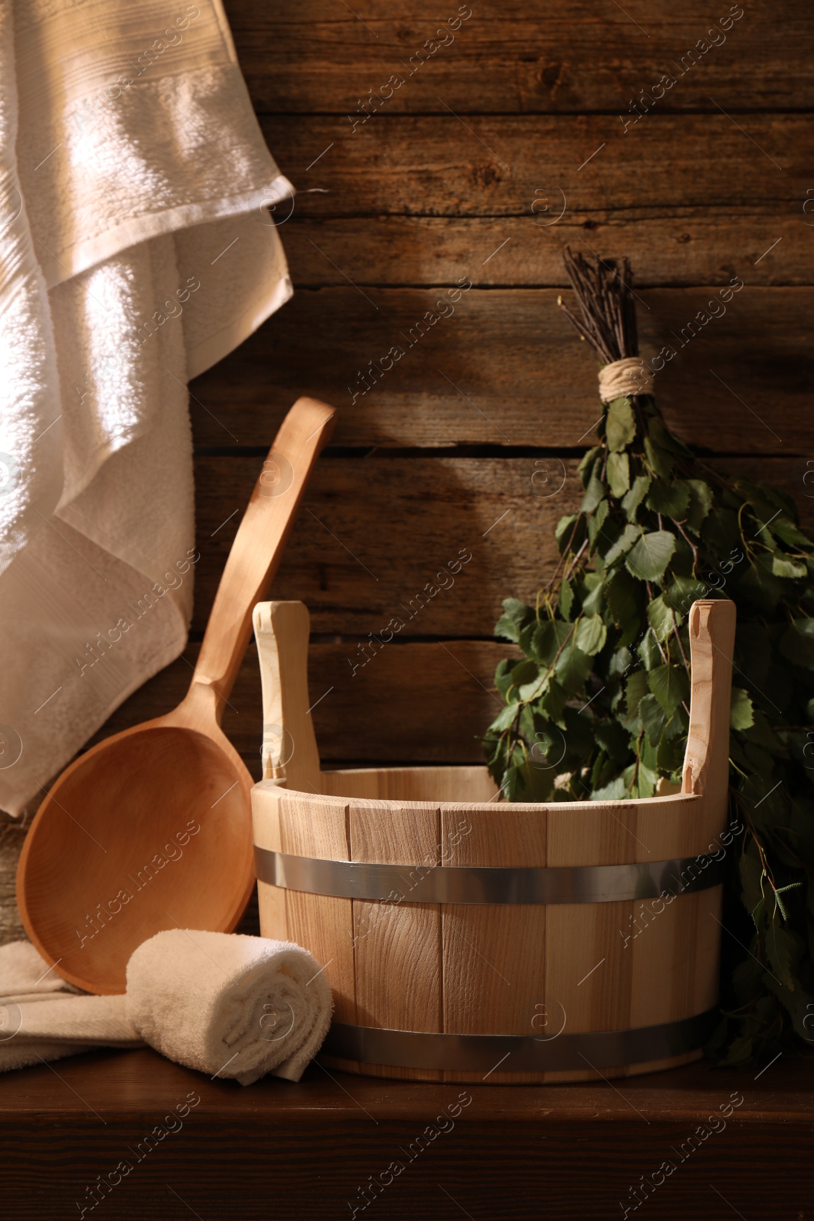 Photo of Sauna equipment. Bucket, ladle, birch whisk and towels on wooden table indoors