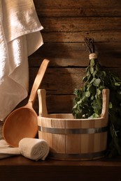 Photo of Sauna equipment. Bucket, ladle, birch whisk and towels on wooden table indoors