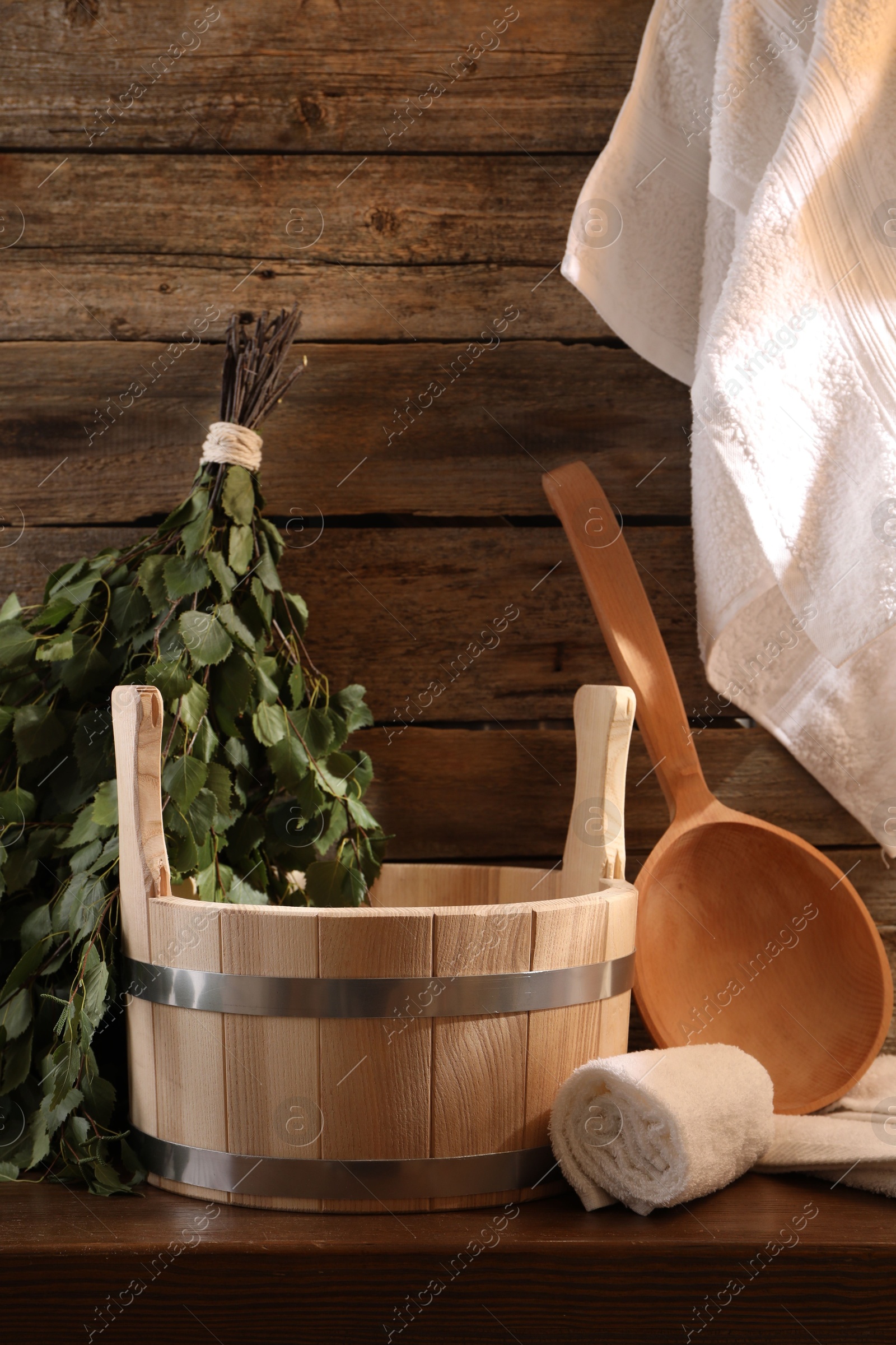 Photo of Sauna equipment. Bucket, ladle, birch whisk and towels on wooden table indoors