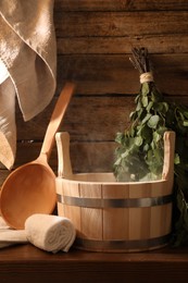 Photo of Sauna equipment. Bucket, ladle, birch whisk and towels on wooden table indoors