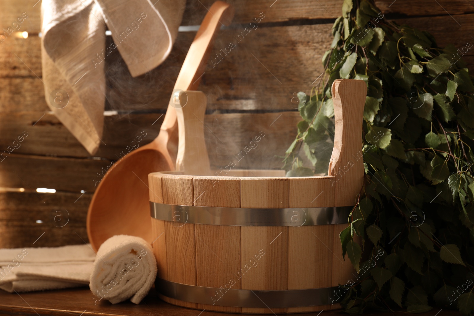 Photo of Sauna equipment. Bucket, ladle, birch whisk and towels on wooden table indoors