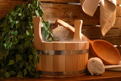 Photo of Sauna equipment. Bucket, ladle, birch whisk and towels on wooden table indoors