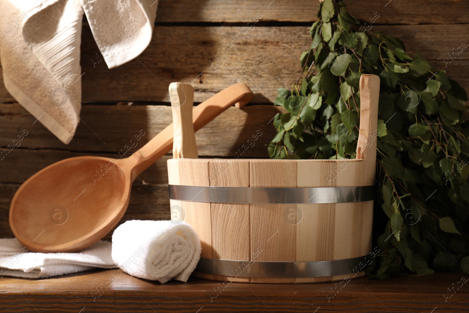 Photo of Sauna equipment. Bucket, ladle, birch whisk and towels on wooden table indoors