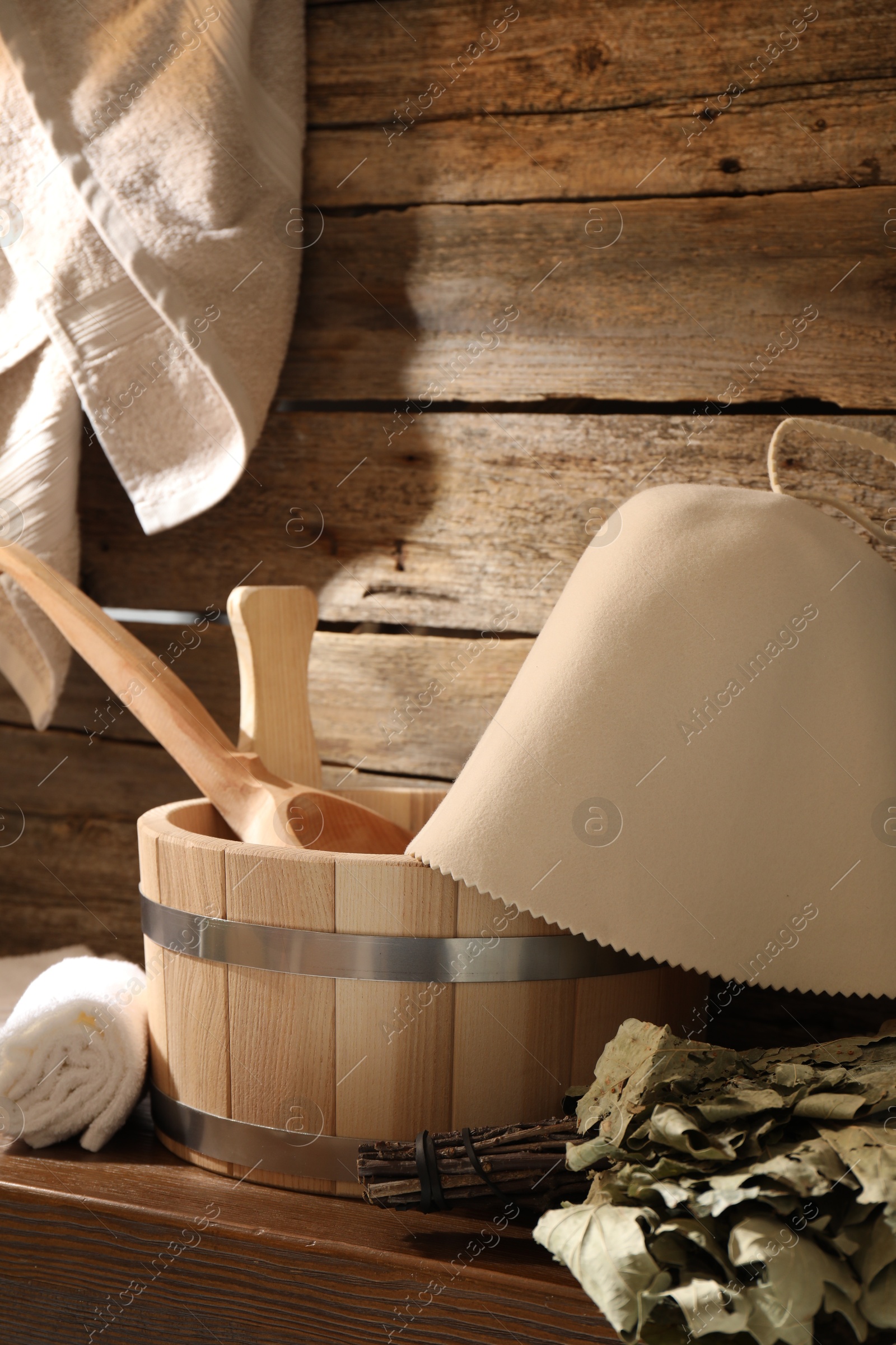 Photo of Sauna equipment. Bucket with ladle, felt wool hat, oak whisk and towels on wooden table indoors