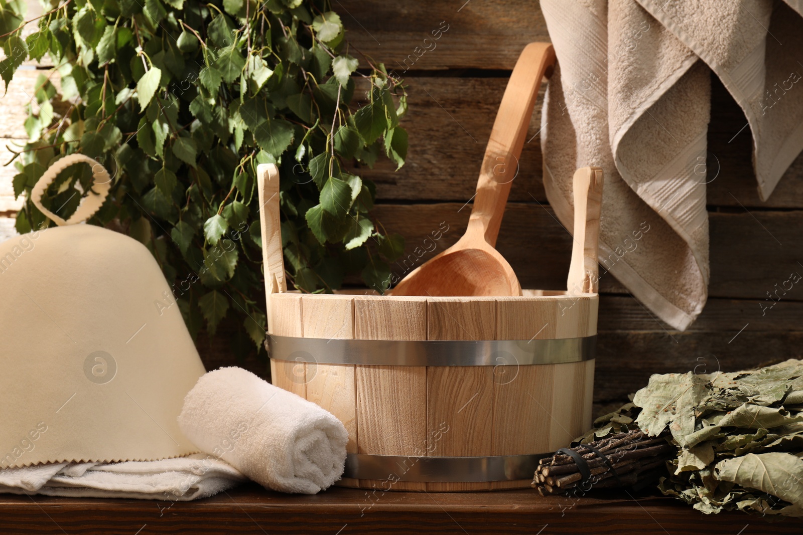 Photo of Sauna equipment. Bucket with ladle, felt wool hat, towels and whisks on wooden table indoors