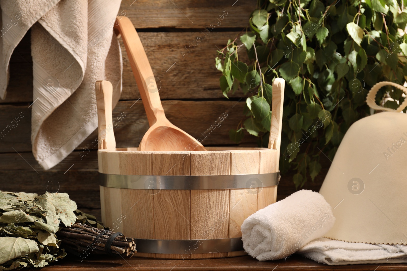 Photo of Sauna equipment. Bucket with ladle, felt wool hat, towels and whisks on wooden table indoors