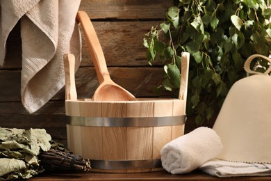 Sauna equipment. Bucket with ladle, felt wool hat, towels and whisks on wooden table indoors