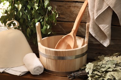 Sauna equipment. Bucket with ladle, felt wool hat, towels and whisks on wooden table indoors