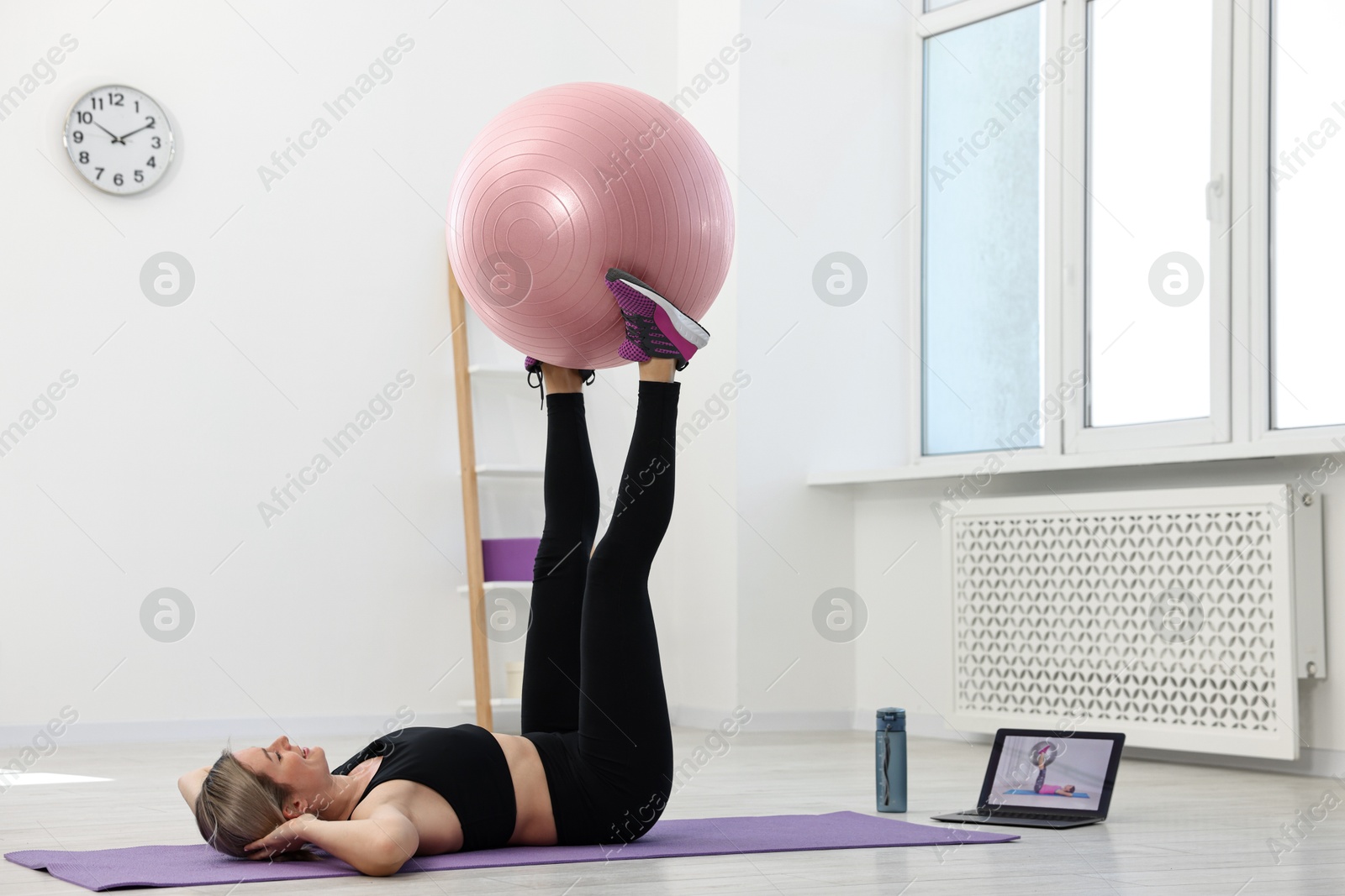 Photo of Online fitness trainer. Woman doing exercise with fitness ball near laptop at home