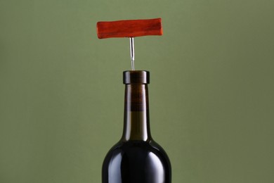 Photo of Wine bottle with corkscrew on olive background, closeup