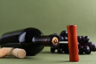 Photo of Wine bottle with corkscrew and corks on olive background, closeup