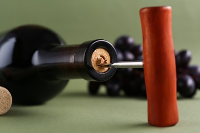 Photo of Wine bottle with corkscrew on olive background, closeup