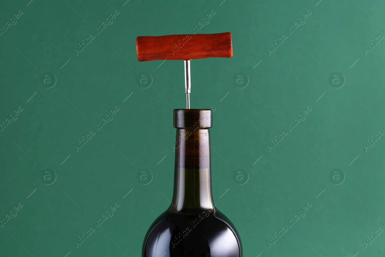 Photo of Wine bottle with corkscrew on green background, closeup