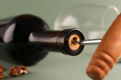 Wine bottle with corkscrew on light grey background, closeup