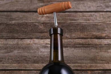 Wine bottle with corkscrew on wooden background, closeup