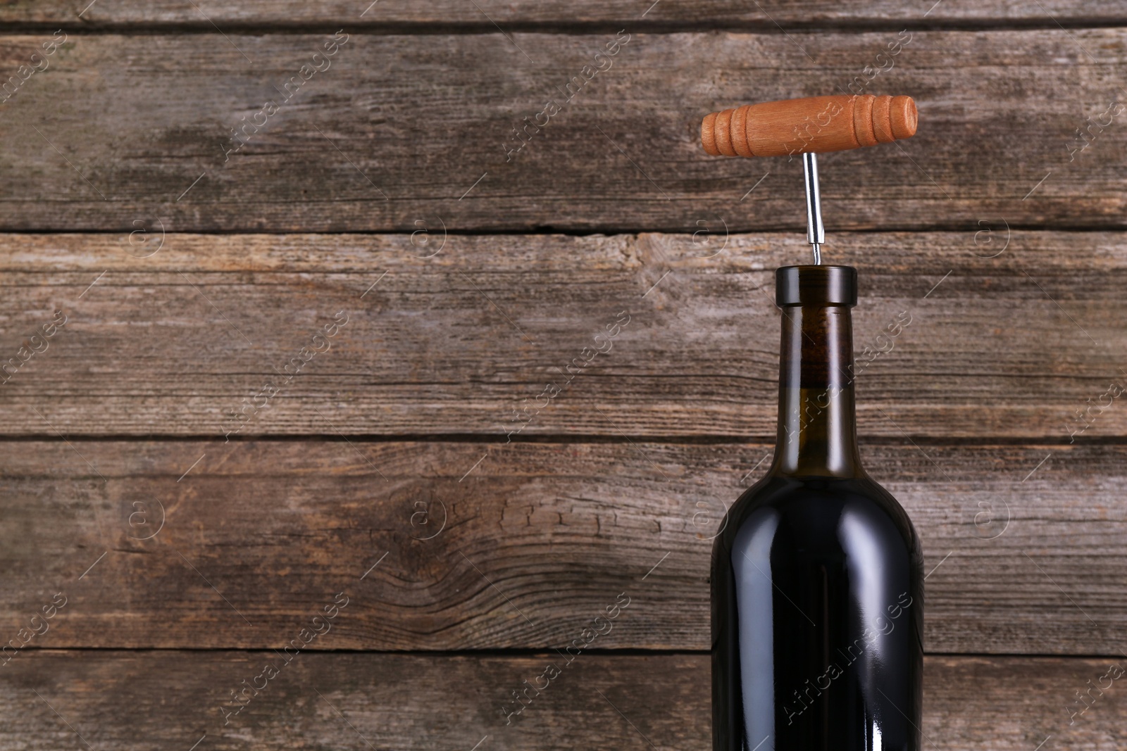 Photo of Wine bottle with corkscrew on wooden background, space for text