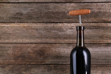 Photo of Wine bottle with corkscrew on wooden background, space for text