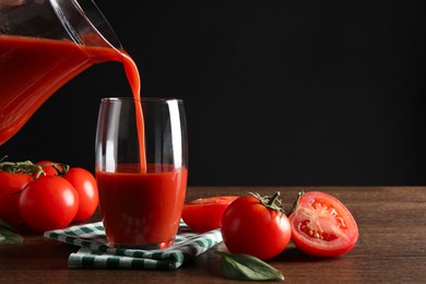 Photo of Pouring tasty tomato juice from jug into glass at wooden table with vegetables. Space for text