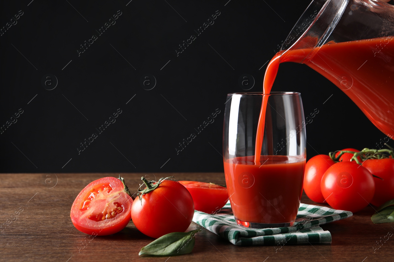 Photo of Pouring tasty tomato juice from jug into glass at wooden table with vegetables. Space for text