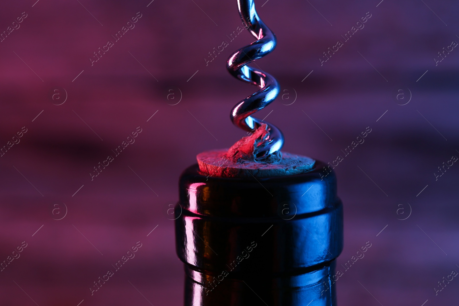 Photo of Wine bottle with corkscrew in lights on dark background, closeup