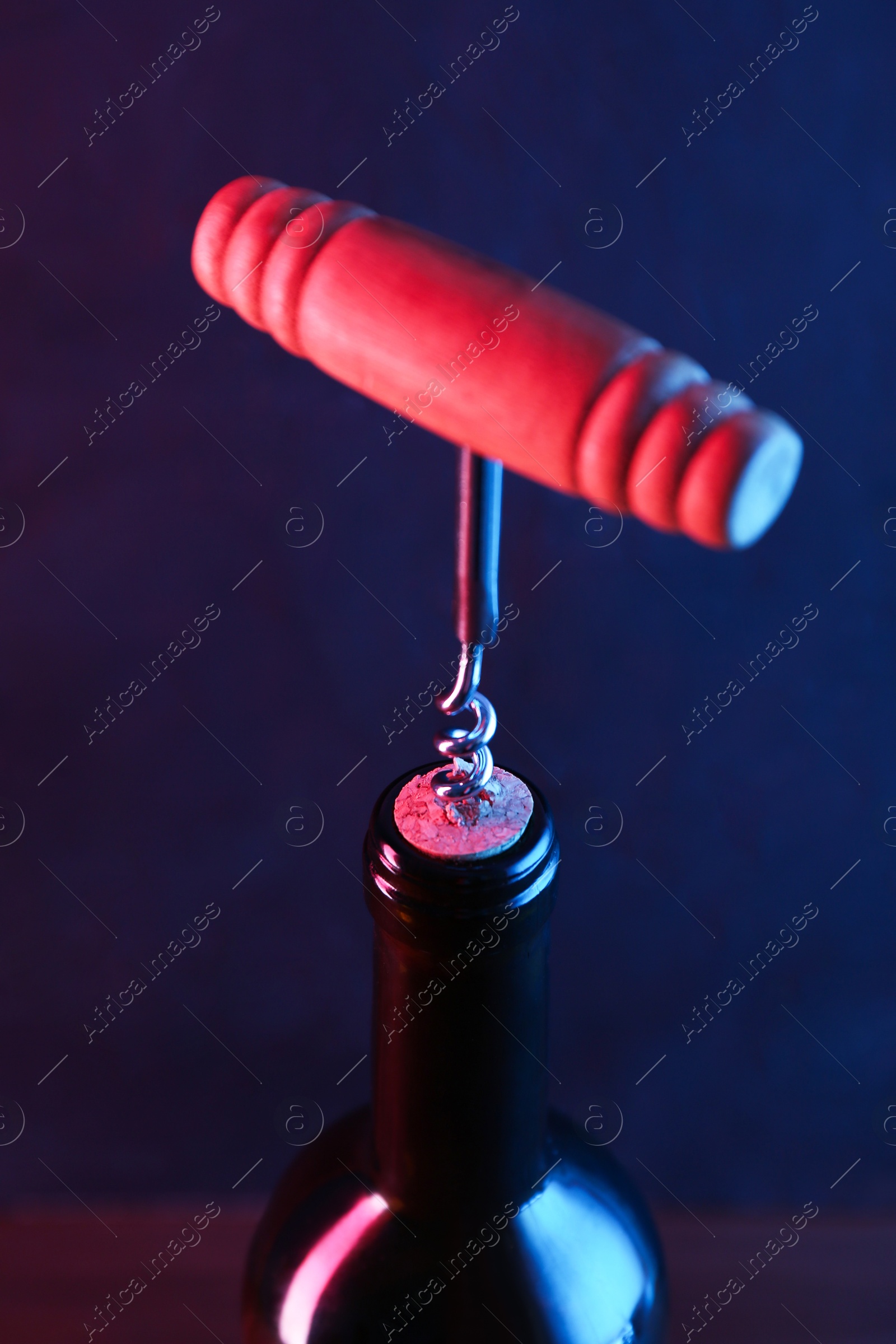 Photo of Wine bottle with corkscrew in lights on dark background, closeup