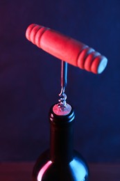 Photo of Wine bottle with corkscrew in lights on dark background, closeup