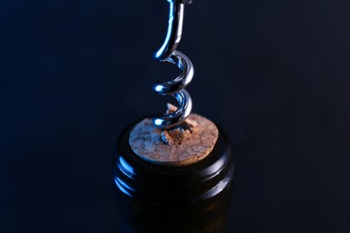 Photo of Wine bottle with corkscrew on dark background, closeup