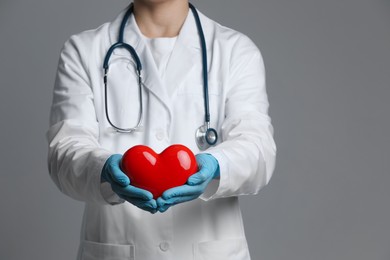 Doctor with red heart on grey background, closeup