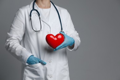 Photo of Doctor with red heart on grey background, closeup. Space for text