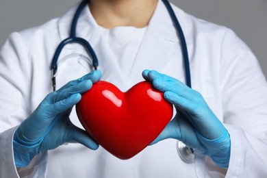 Doctor with red heart on grey background, closeup