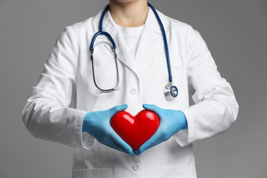 Doctor with red heart on grey background, closeup