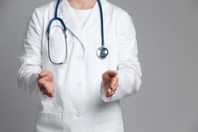 Doctor holding something on grey background, closeup. Space for text