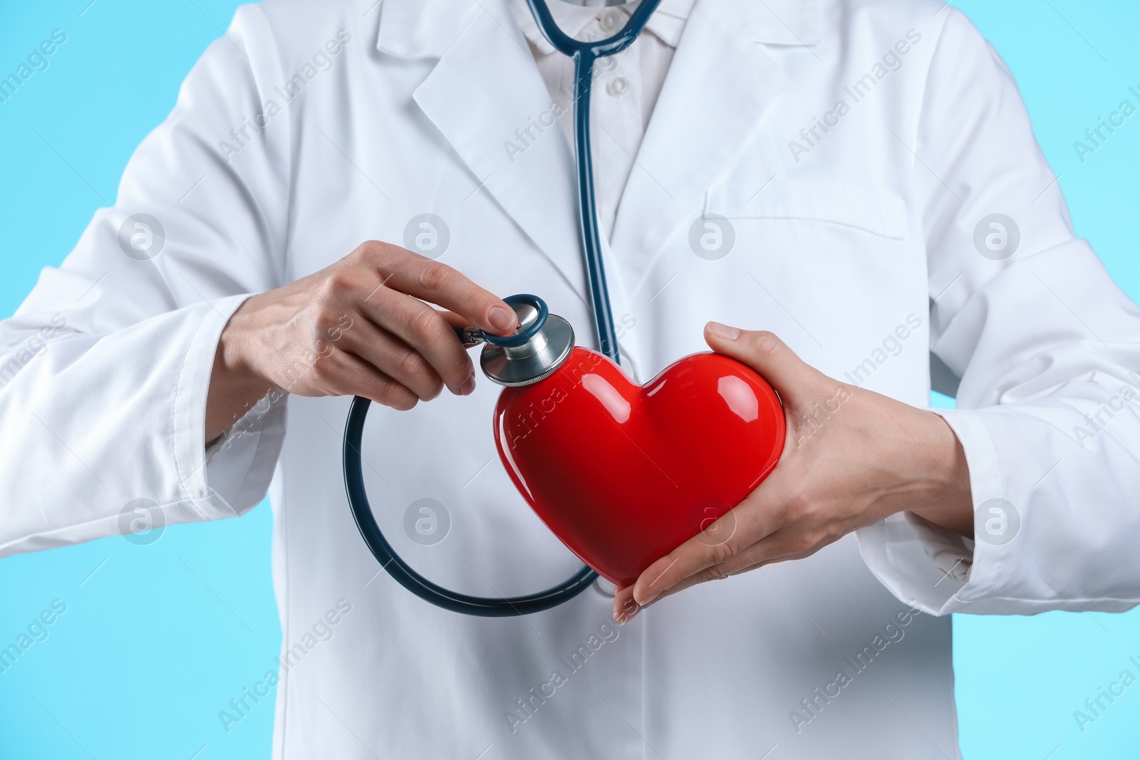 Photo of Doctor with stethoscope and red heart on light blue background, closeup